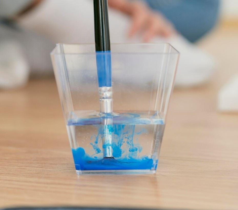 Paintbrush with blue paint in a glass of water